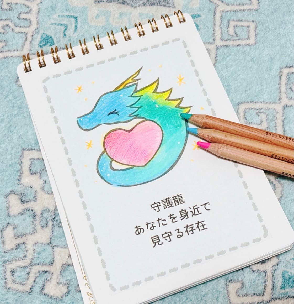 色鉛筆で塗られた青緑の龍とハートの絵。添え書き「守護龍 あなたを身近で見守る存在」と色鉛筆3本